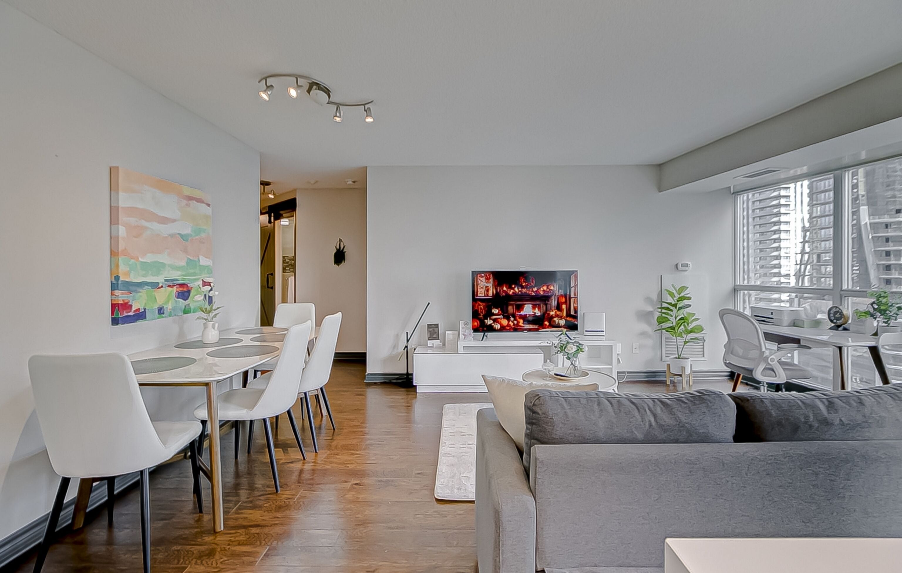 Una sala de estar moderna con comedor, un sofá gris, televisor y un ventanal grande.