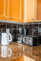 A kitchen with wooden cabinets, a coffee maker, a blender, and a toaster on a granite countertop.