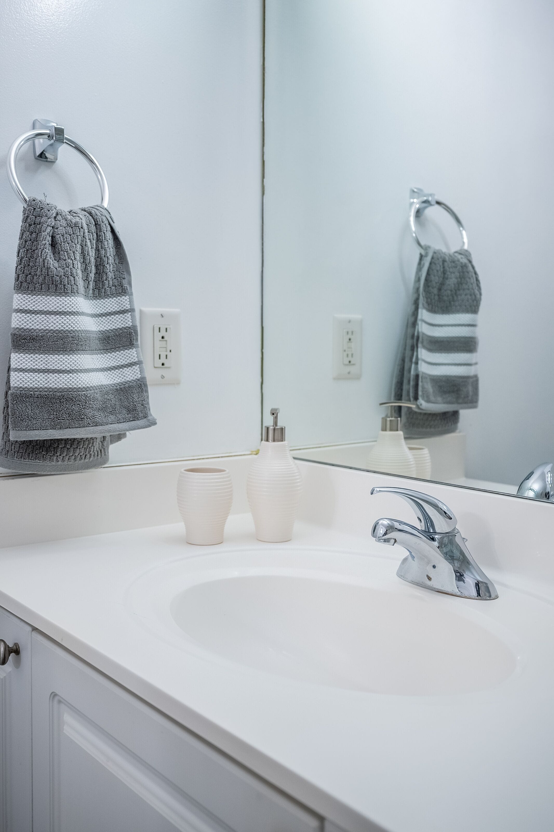 A bathroom with a white sink, a mirror, and two towels hanging on towel rings.