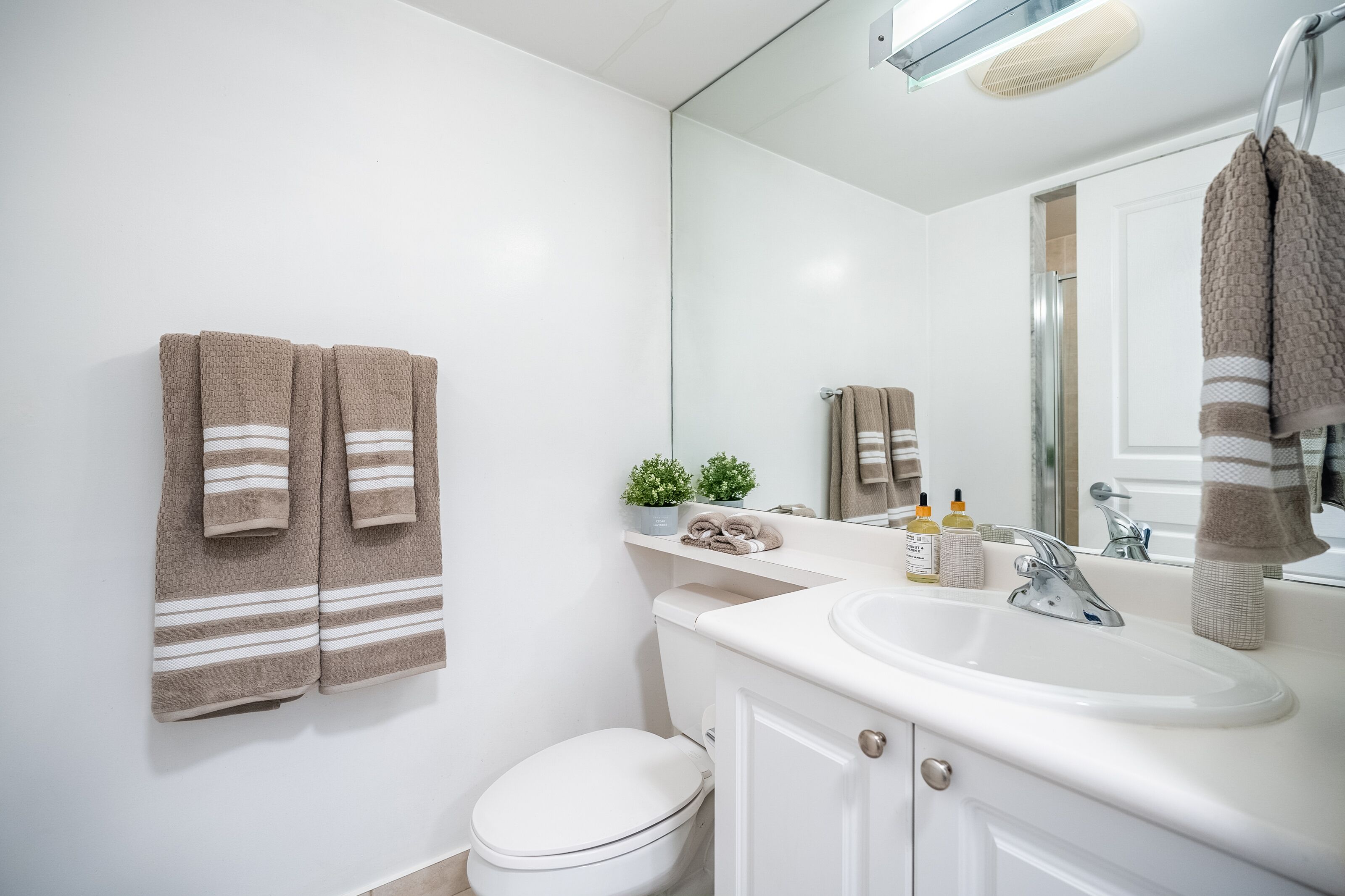 A bathroom with a white toilet, a sink with a mirror, and two towels hanging on the wall.