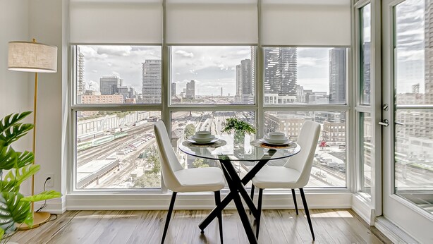 Un coin repas avec une table en verre et deux chaises, une lampe, et une vue sur le paysage urbain à travers de grandes fenêtres.