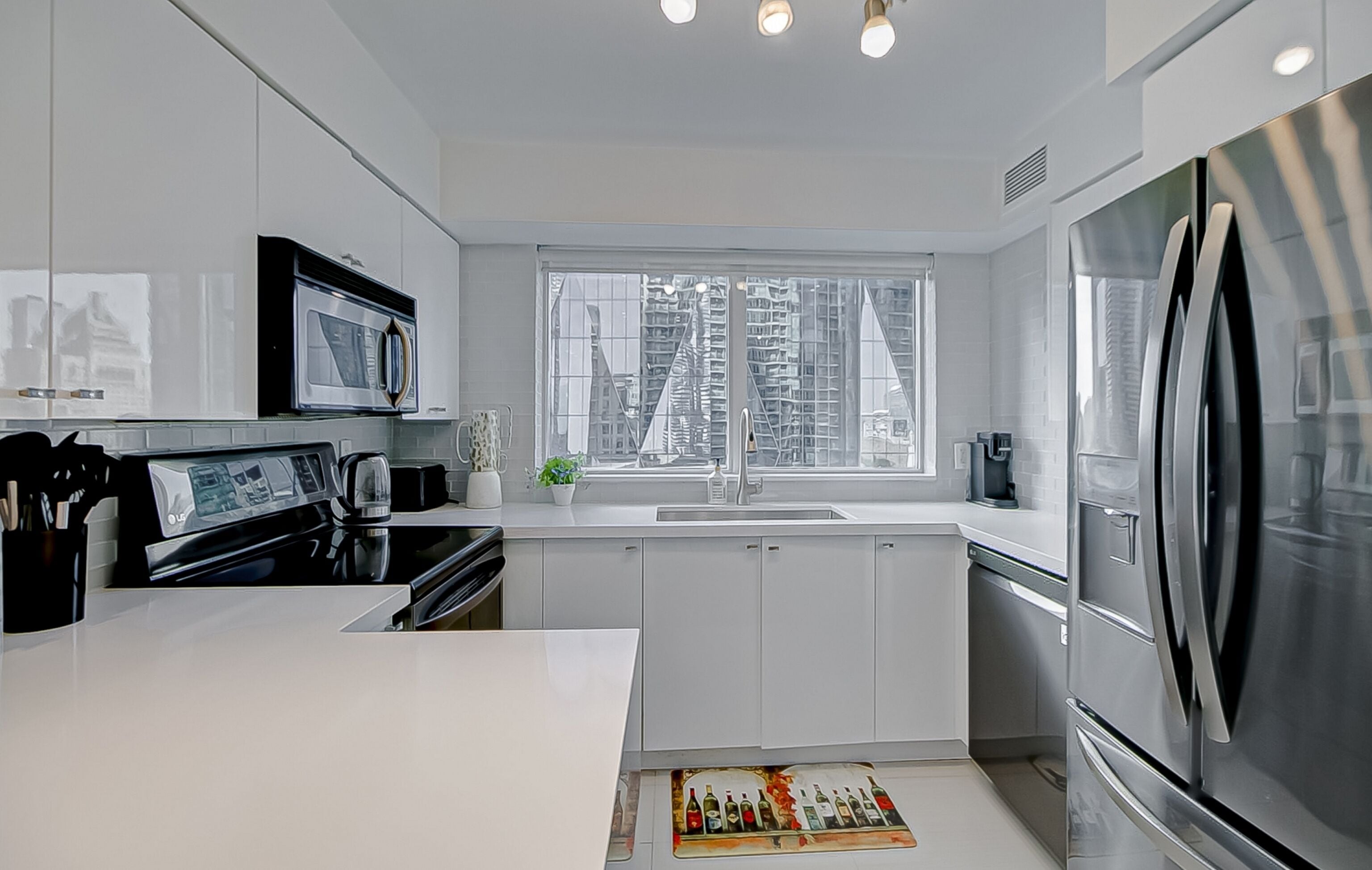 A modern kitchen with white cabinetry, stainless steel appliances, and a large window offering a city view.