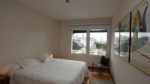 Ein Schlafzimmer mit einem Bett, einem Sessel und einem großen Fenster mit Blick auf die Stadt.