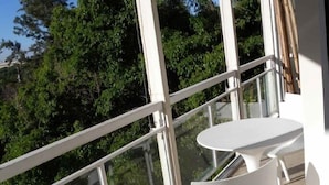Ein Balkon mit Glastrennwand, einem weißen Tisch und zwei weißen Stühlen.