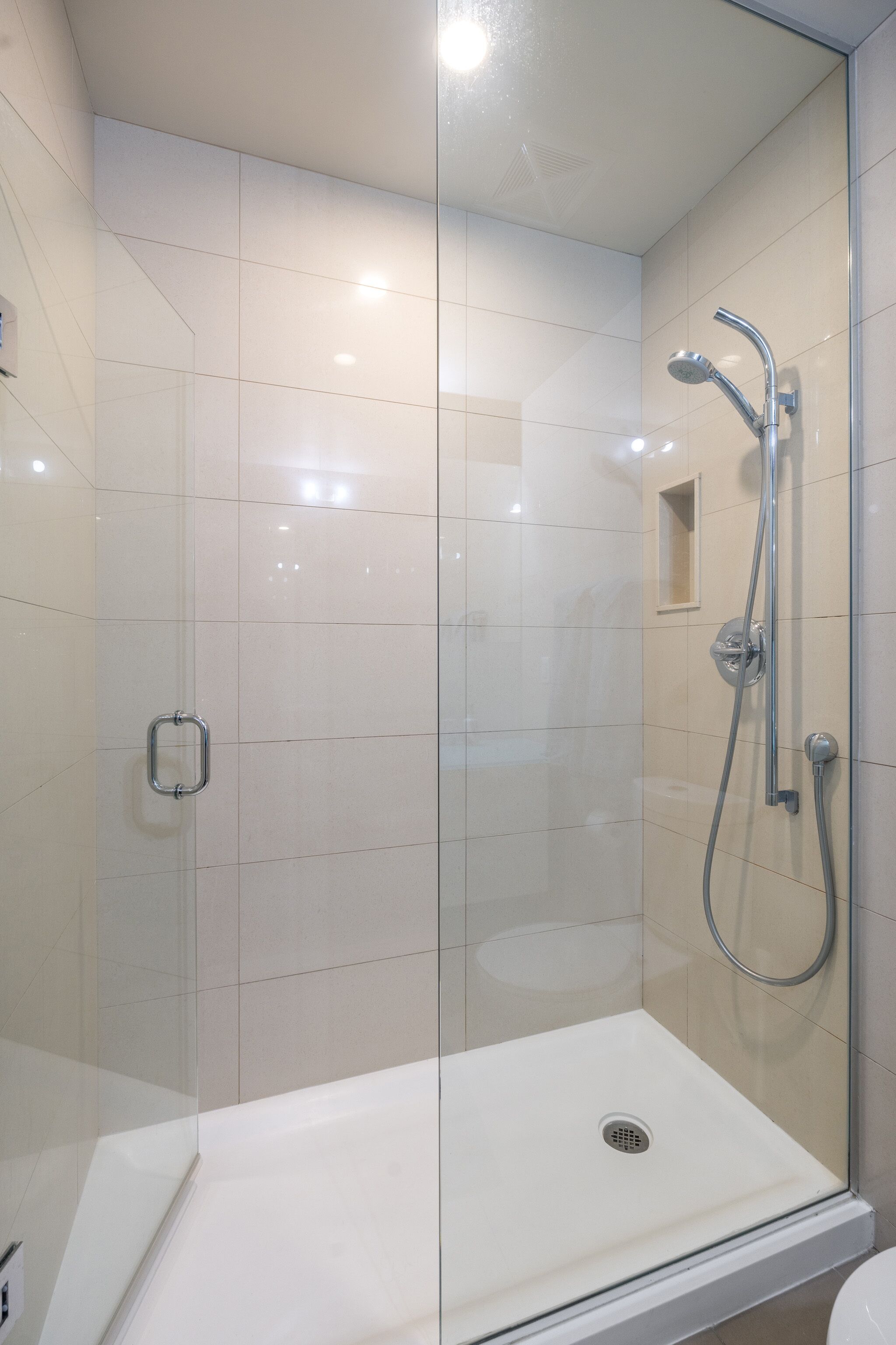 Un baño moderno con ducha acristalada, lavabo blanco y suelo de baldosas.