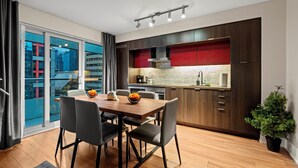 A modern kitchen with dark wood cabinets, a red backsplash, and a dining area with a wooden table and chairs. - Modern Downtown Apartments (Toronto)