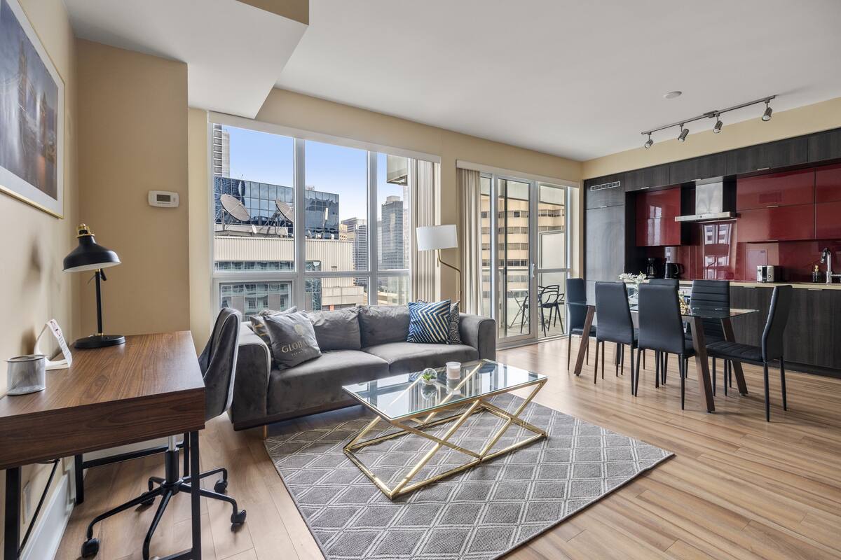 A modern living room with a glass coffee table, a sofa, and a dining area with chairs.
