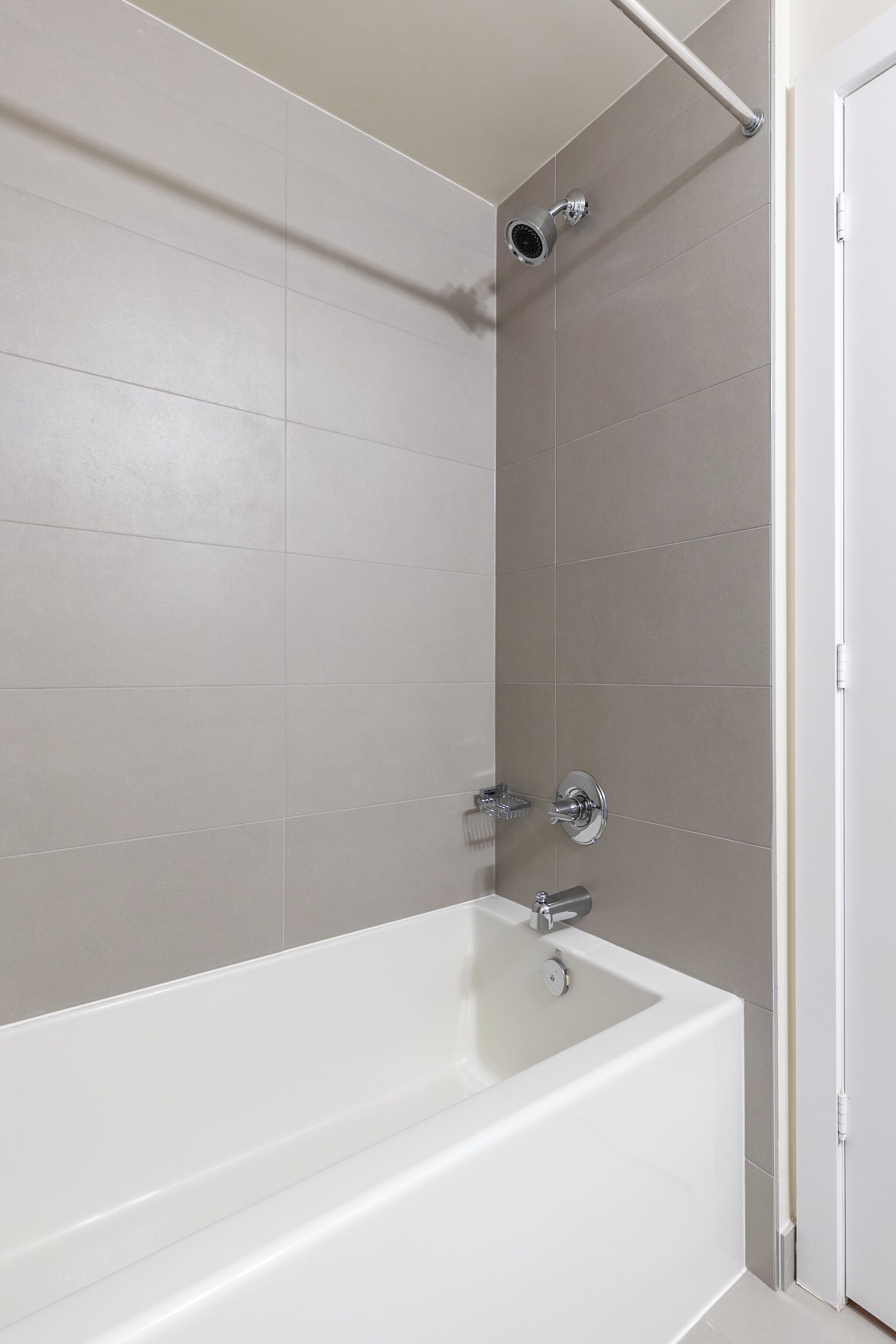 A modern bathroom with a white bathtub, a showerhead, and a door.
