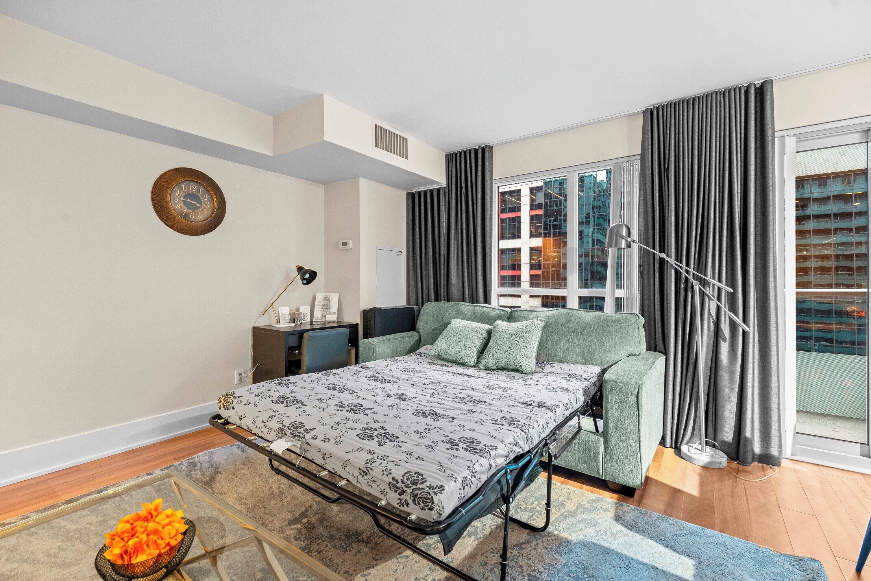 A modern bedroom with a bed, a desk, and a view of the city through large windows.