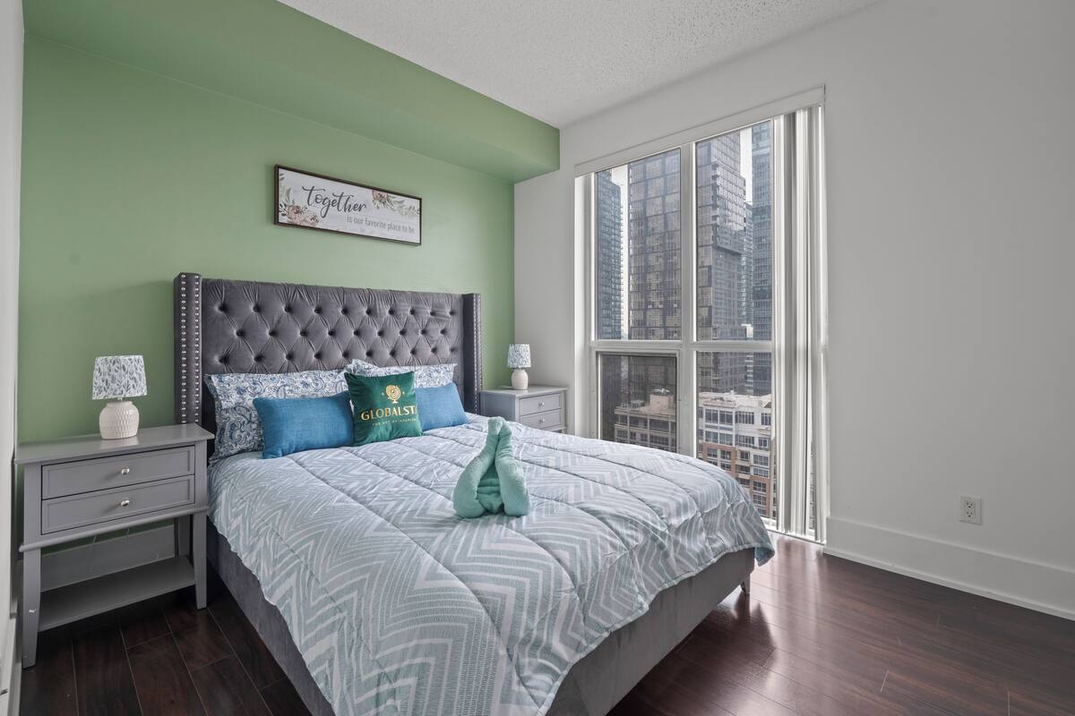 A bedroom with a large bed, green walls, a city view, and a framed quote on the wall.