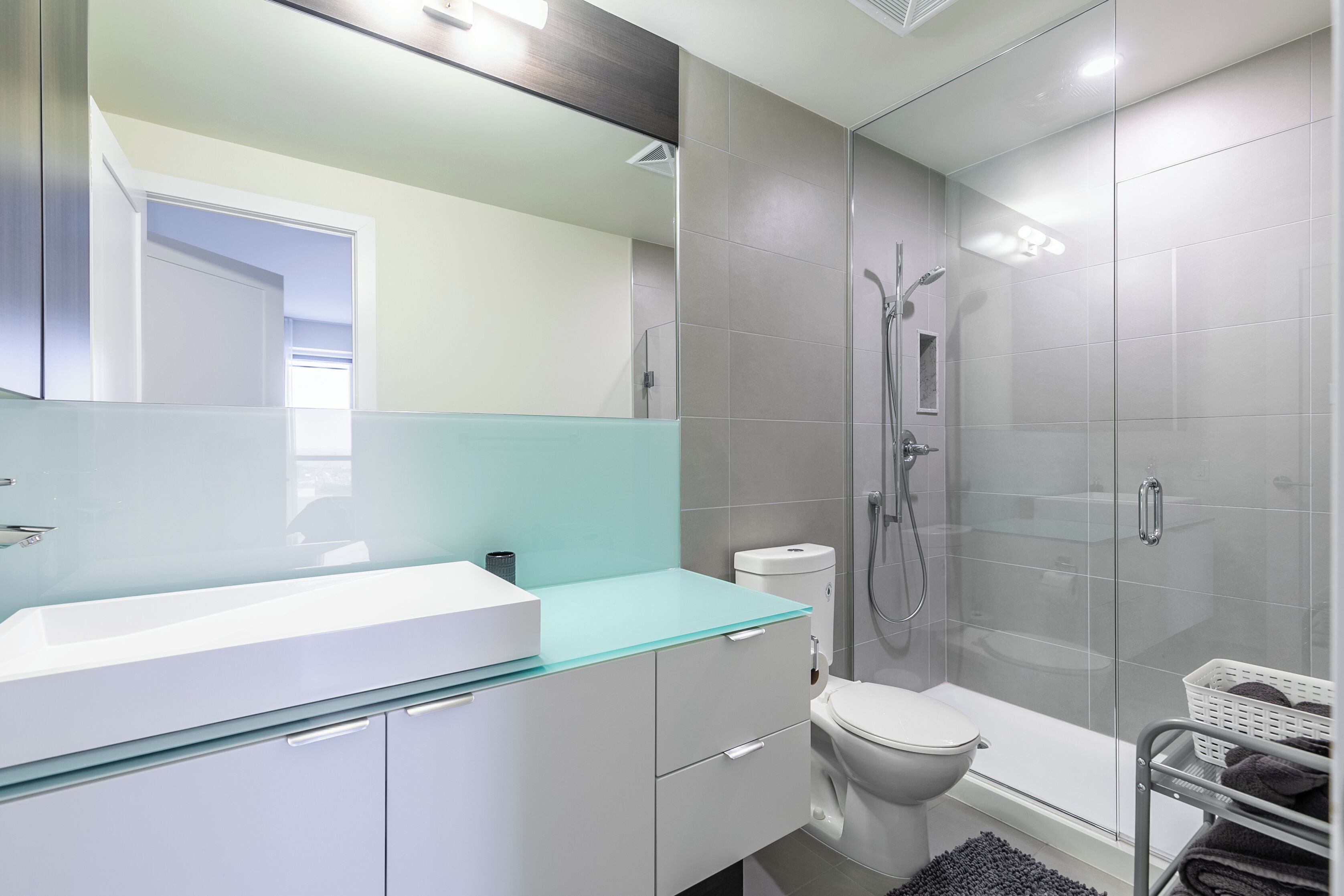 A modern bathroom with a glass sink, white cabinets, a toilet, a glass shower enclosure, and a white towel rack.