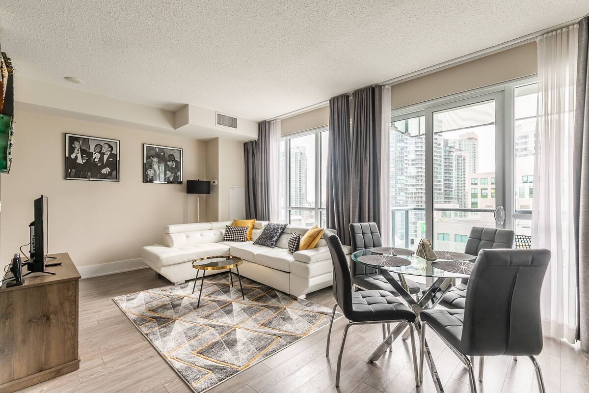 A modern living room with a white sofa, a glass dining table, and a view of high-rise buildings.