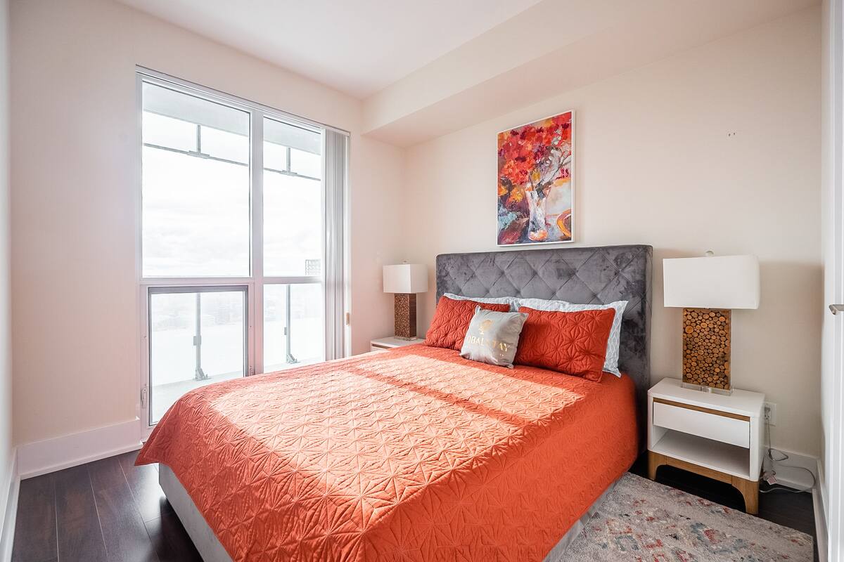 A bedroom with a large bed, two bedside tables, a window, and a painting on the wall.