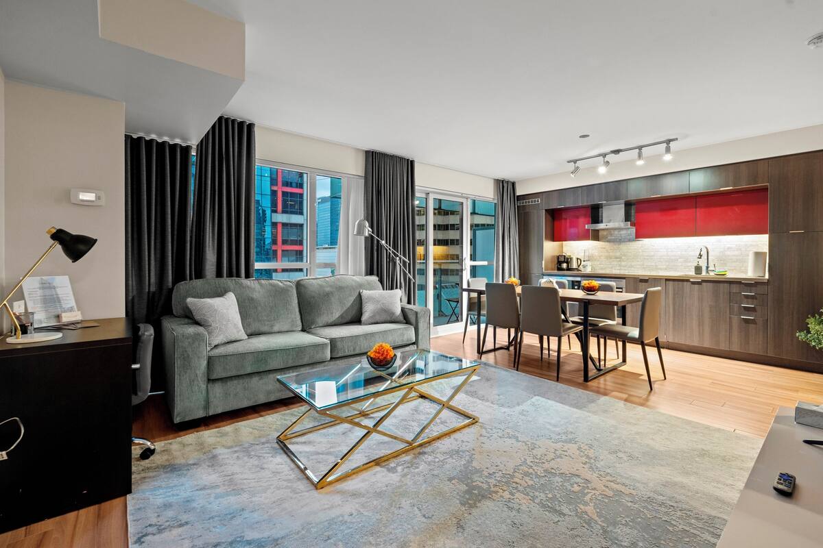 A modern living room with a grey sofa, a glass coffee table, and a dining area with a wooden table and chairs.