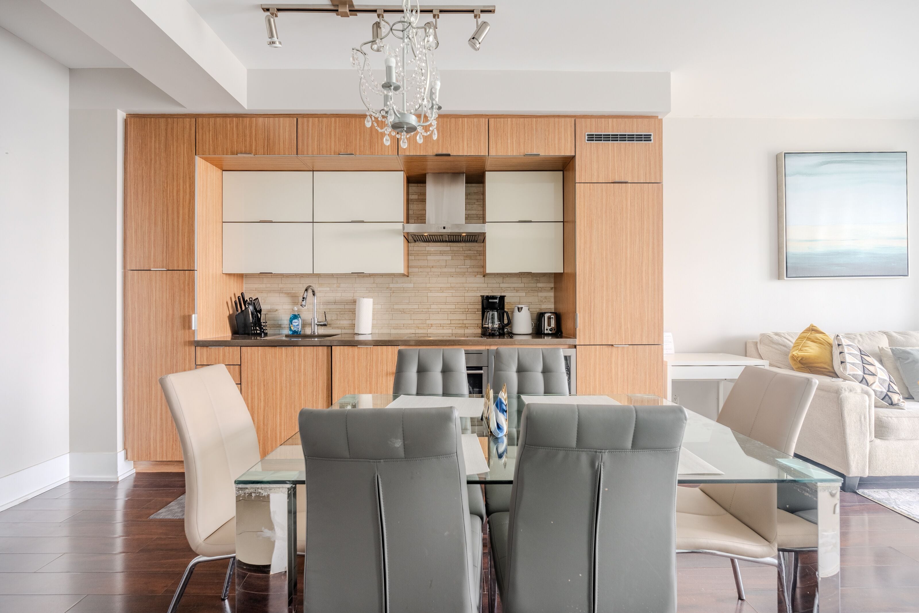 Een moderne keuken met houten kastjes, een glazen eettafel en grijze stoelen.