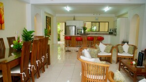 A spacious living area with a dining table, multiple chairs, a sofa, and a kitchen in the background.