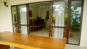 A dining area with a wooden table and chairs, a glass door leading to a dining room, and a ceiling fan.