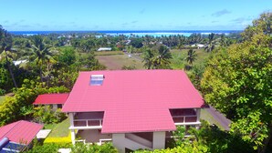 A two-story building with a red roof, surrounded by lush greenery and a view of the ocean.