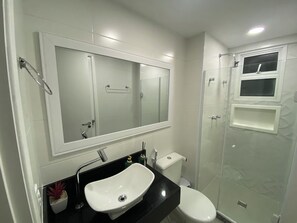 A modern bathroom with a large mirror, a sink, a toilet, and a glass-enclosed shower.