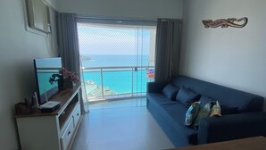 Una sala de estar con sofá, televisor y balcón con vista al mar.