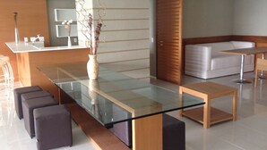 Un moderno vestíbulo de hotel con una mesa de vidrio, asientos acolchados, un banco de madera y una zona de recepción con mostrador y bar.
