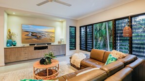 Una sala de estar moderna con un sofá de cuero, televisor y un ventanal con vista a palmeras.