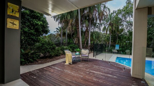 Una terraza de madera con mobiliario exterior, piscina y jardín tropical.