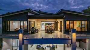 Una casa moderna de dos pisos con un patio cubierto, un comedor y una cocina a la vista a través de las puertas abiertas.