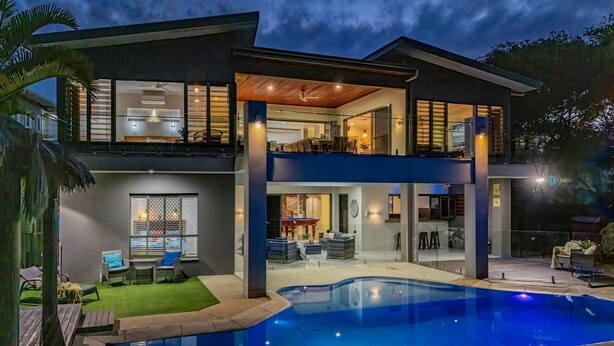 Una casa moderna de dos pisos con piscina, ventanas amplias y un balcón.