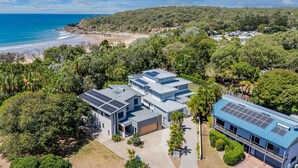 Una casa moderna con paneles solares, rodeada de exuberante vegetación y una playa.