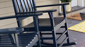 A black rocking chair in front of a house with a sign that reads "The Nest" and a small potted plant beside the door. - The Nest Hudson (Hudson)