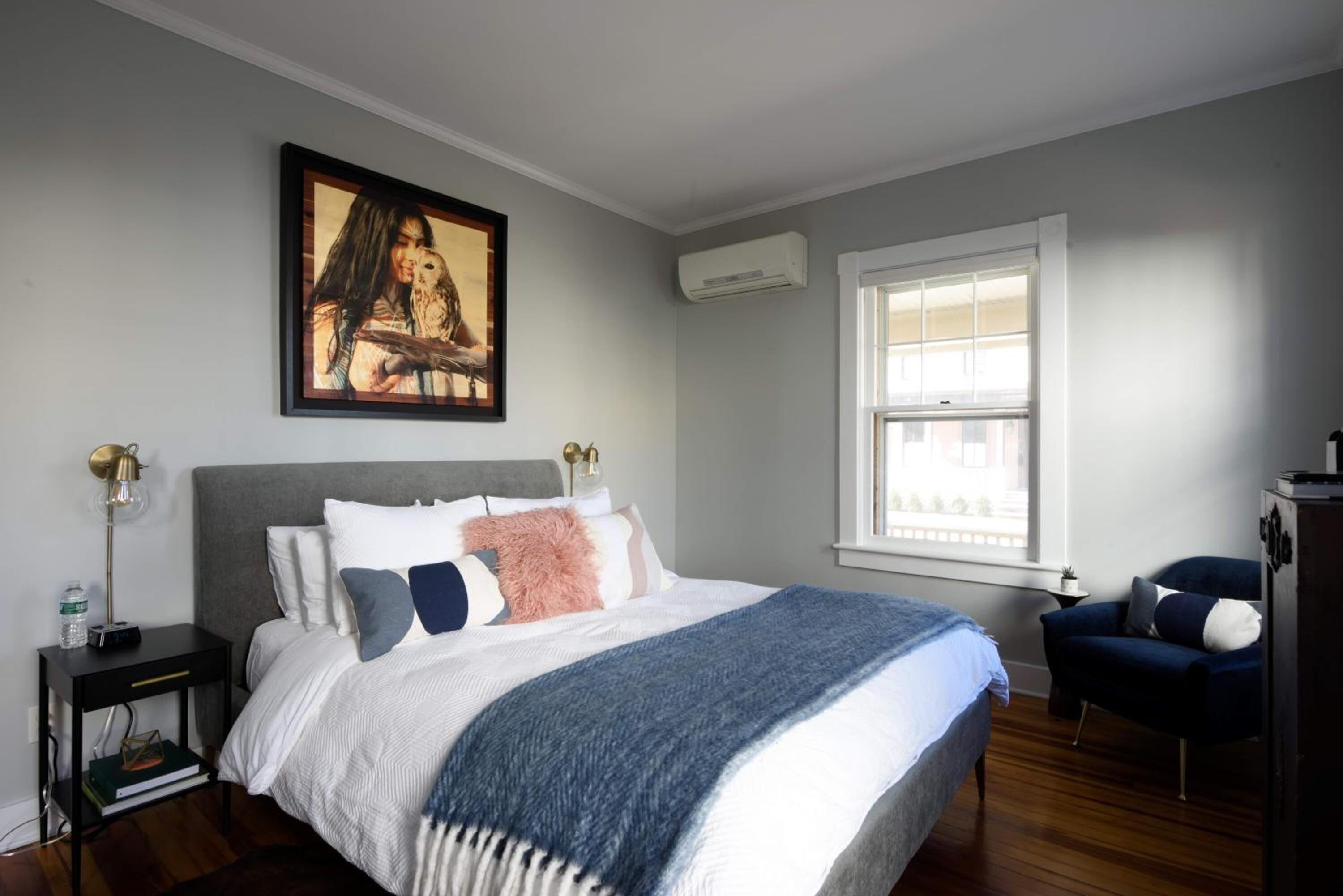A bedroom with a bed, a nightstand, a chair, a window, and a painting on the wall.