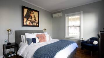 A bedroom with a bed, a nightstand, a chair, a window, and a painting on the wall.