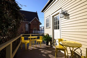 A wooden deck with yellow chairs and a table, a white building with a window and a door, and a brick building in the background. - The Nest Hudson (Hudson)