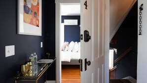 A hallway with a bed in the background, a door with the number 4, and a small table with water bottles and a coffee maker. - The Nest Hudson (Hudson)