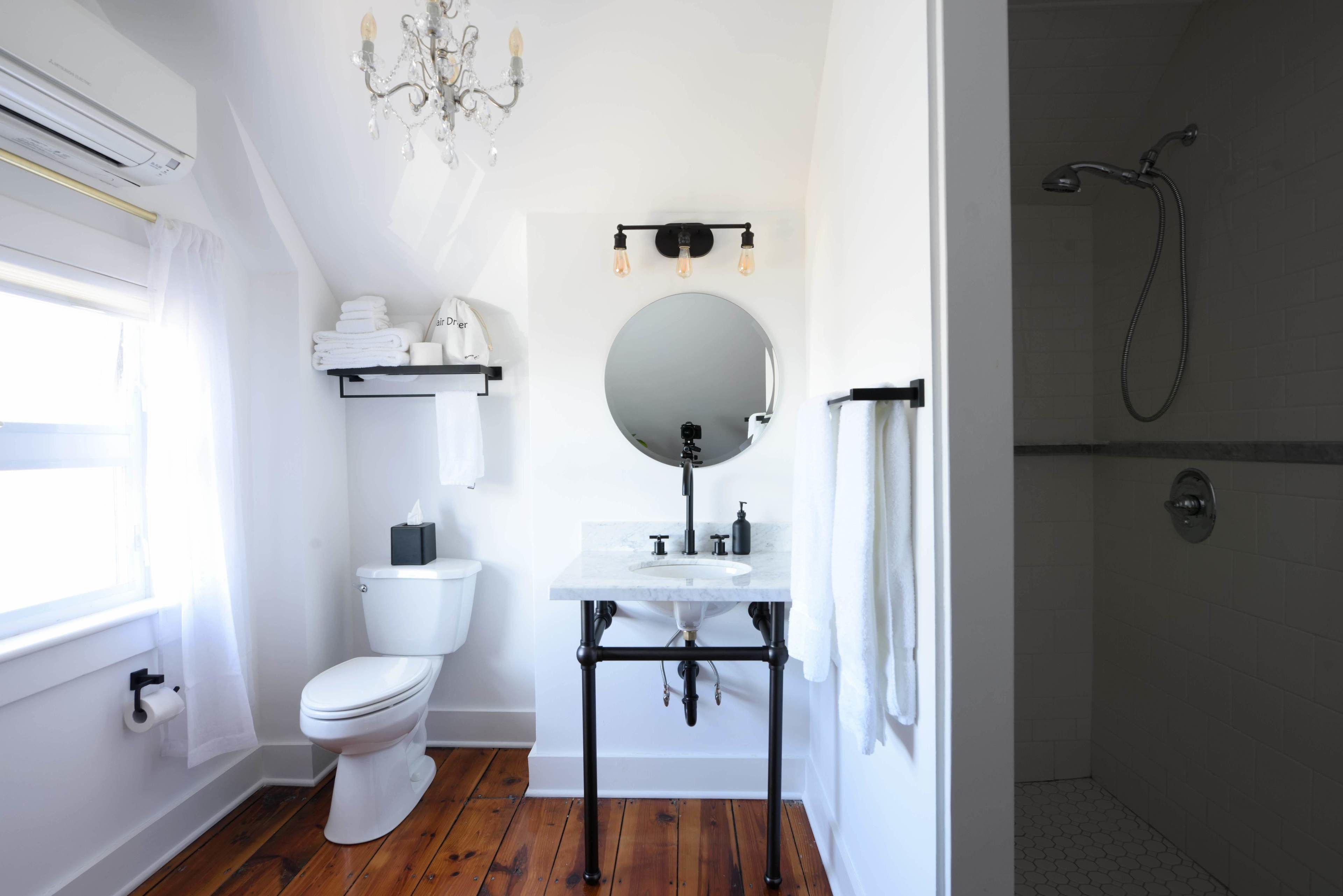 Un baño con inodoro blanco, lavamanos con espejo, ducha y candelabro.