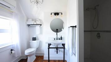 Un baño con inodoro blanco, lavamanos con espejo, ducha y candelabro.