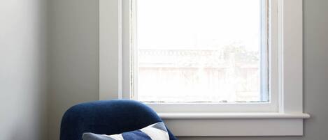 A corner room with a blue armchair, a small side table with a plant, and a window with a view of buildings.