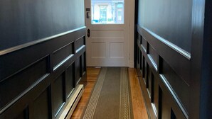 A hallway with dark walls, a patterned rug, and a door leading to a bright room. - The Nest Hudson (Hudson)