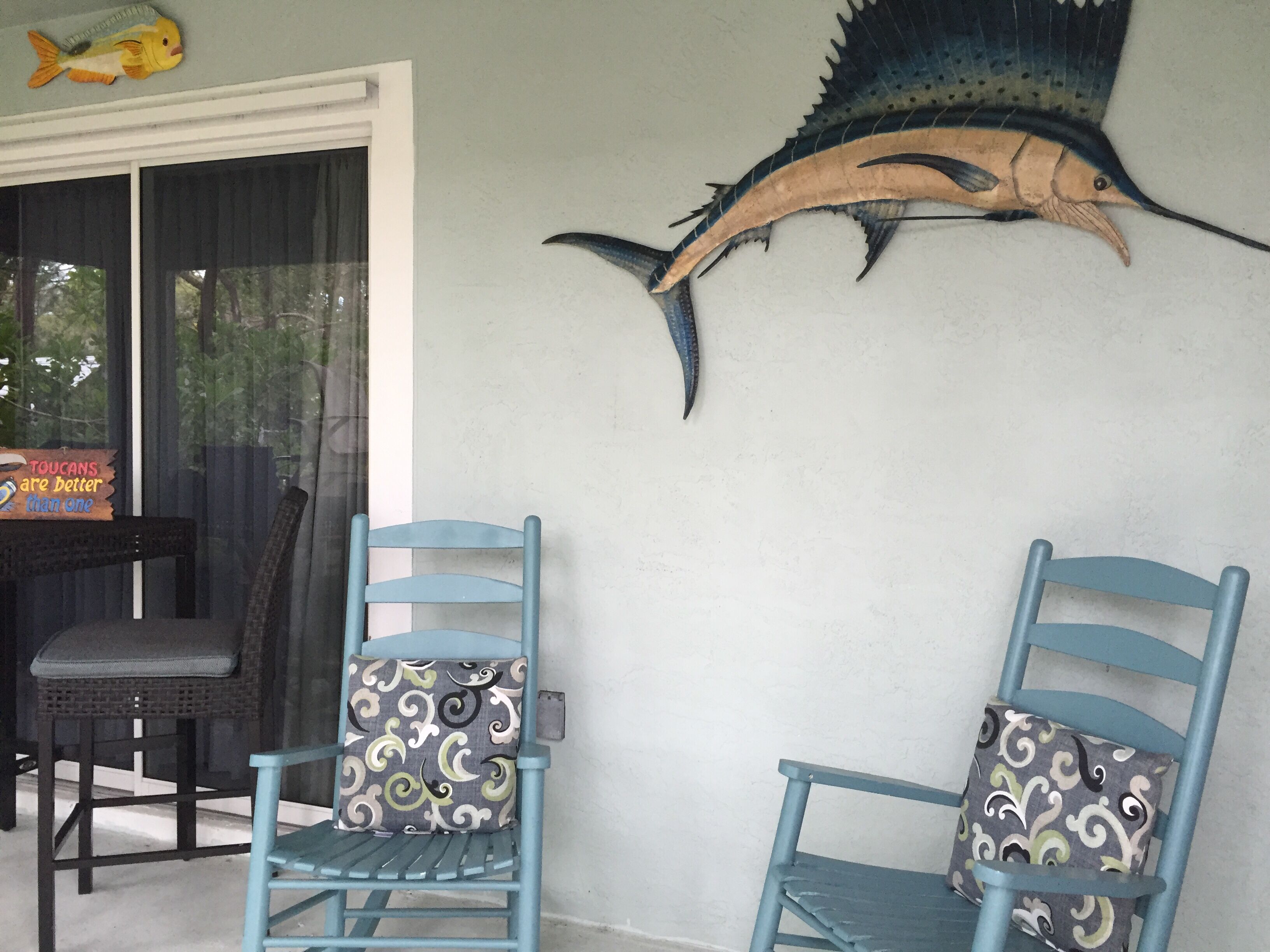 A room with two blue chairs with patterned cushions, a large fish mural on the wall, and a sign that reads "TOUCANS are better than one".