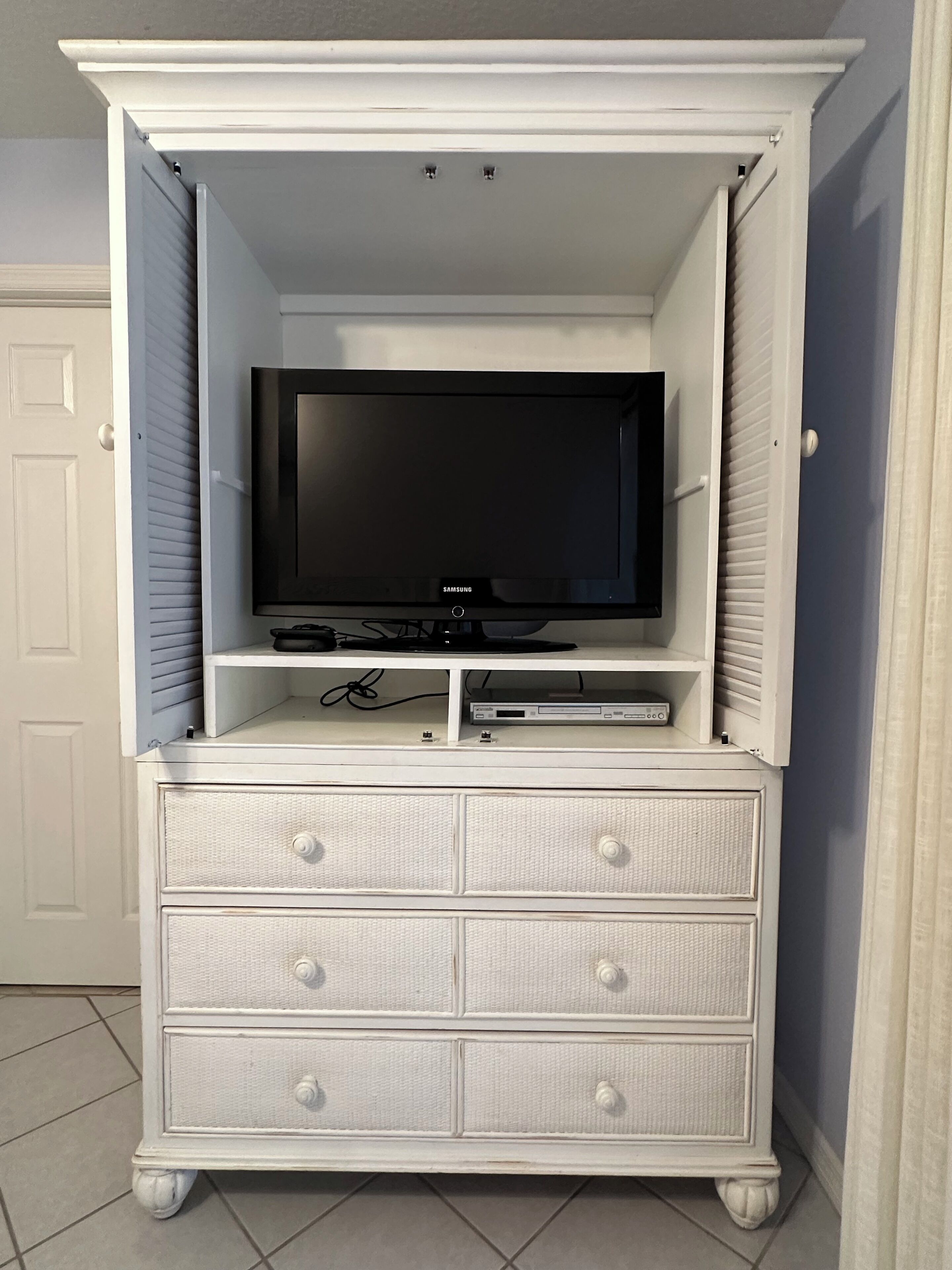 A white entertainment center with a flat-screen TV, a DVD player, and a shelf.