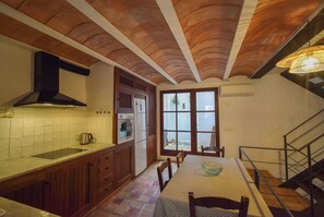 A kitchen with wooden cabinets, a black range hood, a window, and a dining table with chairs. - Charming townhouse, walking distance from the main square (Sóller)