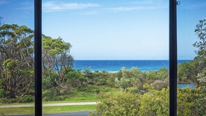 A coastal view with a clear sky, trees, and a pathway leading to the beach. - Yabbarra Sands - Enjoy the beachside lifestyle- Close to Surf, MBT and Whales! (Dalmeny)