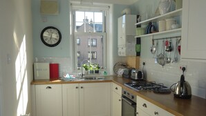 Una cocina con armarios blancos, encimera de madera, estufa a gas y ventana con vistas a edificios.
