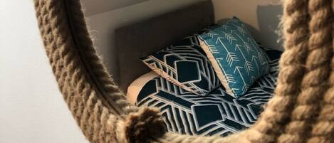 A round mirror with a rope frame, reflecting a bed with patterned pillows and a geometric wall design.