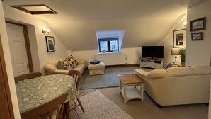 A cozy living room with a dining table, two sofas, a TV, and a window with a view. - Large Traditional Stone 3 Bedroom 1ST Floor Apartment On The Jurassic Coast. (Langton Matravers)