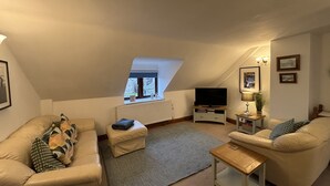 A cozy living room with a sofa, a coffee table, a television, and a small side table. - Large Traditional Stone 3 Bedroom 1ST Floor Apartment On The Jurassic Coast. (Langton Matravers)