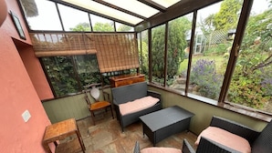 Un solárium con mobiliario de mimbre, una mesita y vistas al jardín.