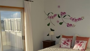 Een slaapkamer met een bed, een nachtkastje, een lamp, een raam met gordijnen en een balkon.