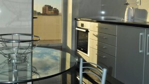 Een moderne keuken met een glazen eettafel en stoelen, een inbouwoven en een uitzicht op de stad door een groot raam.
